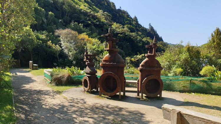 Outdoors photo of a gravel path next to 3 rusty metal historic pumps.